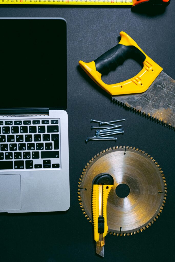 Flat lay of a laptop and various hand tools on a dark surface, perfect for DIY or technology themes.