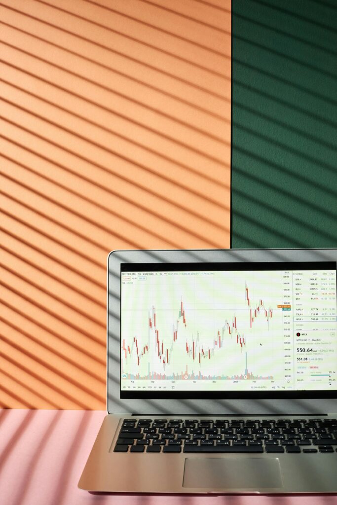 A laptop showing financial graphs with shadow lines against a colorful background, illustrating market analysis.